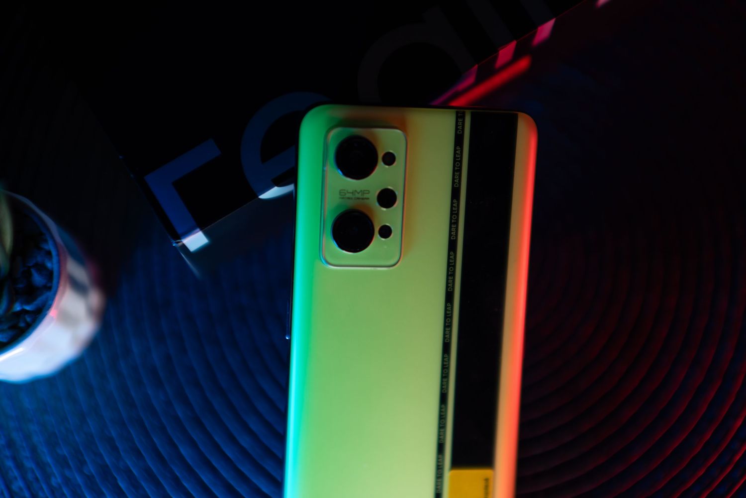 Realme smartphone back view with multi-camera setup under vibrant green and red neon lighting.