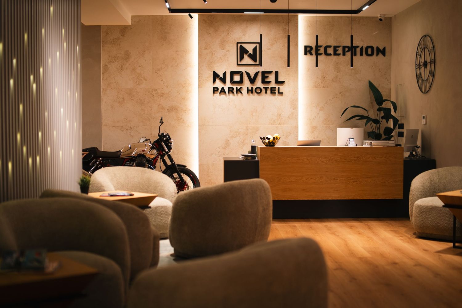 Modern hotel lobby of Novel Park Hotel featuring a reception desk, motorcycle display, and plush seating area.