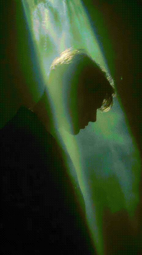 A silhouetted figure bathed in dramatic blue-green light beams creating an ethereal, mysterious atmosphere.