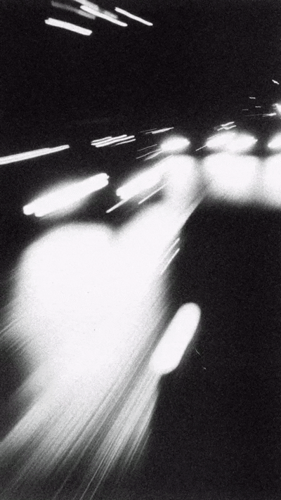 Black and white long exposure photo of cars on a highway at night, with streaking headlights and motion blur.