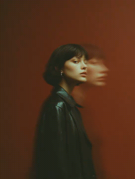 A young woman with a short dark bob stands against a red dotted background with a ghostly double exposure effect.