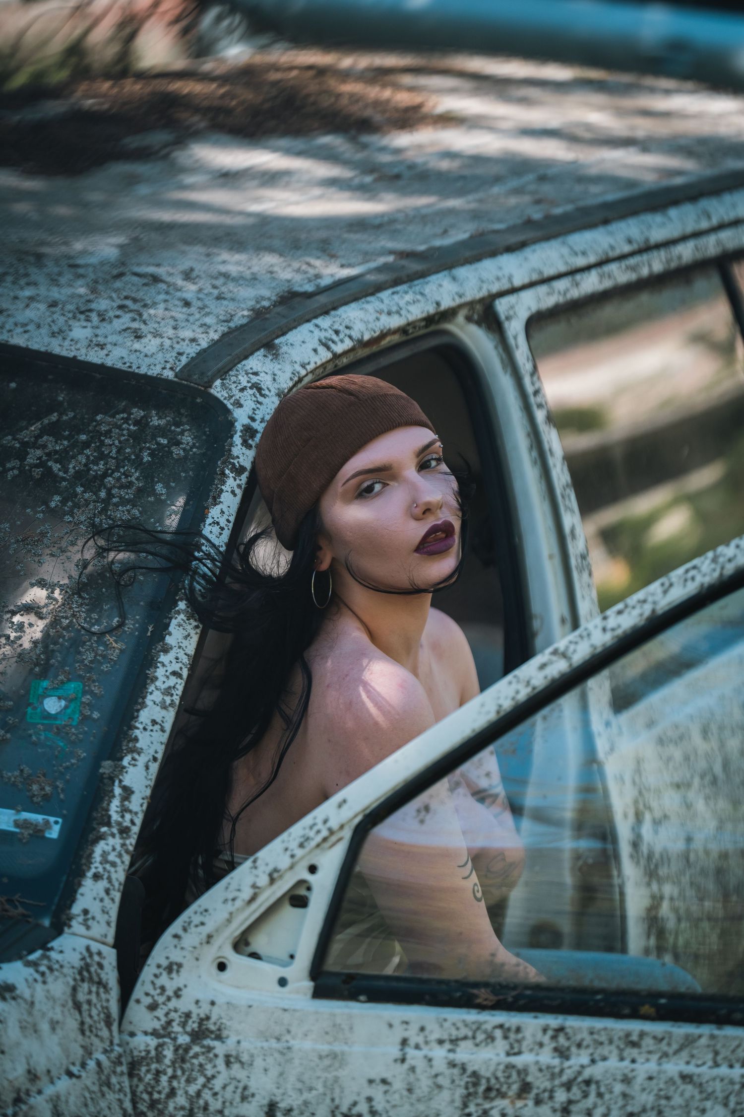 Dramatic portrait of woman with dark lipstick and headscarf looking through window of rusty old car.