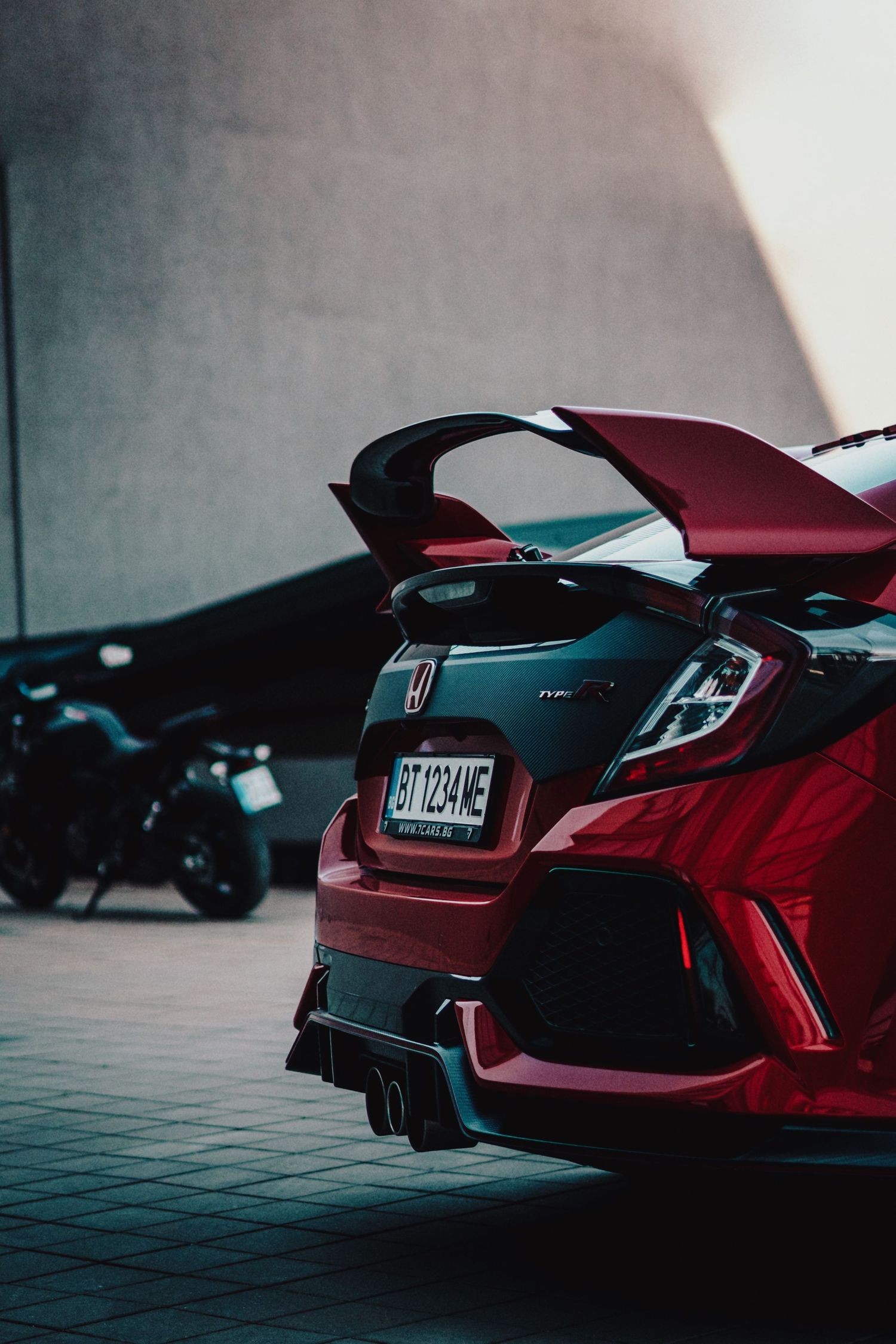 Rear view of a red Honda Civic Type R with spoiler parked in a garage next to a motorcycle.