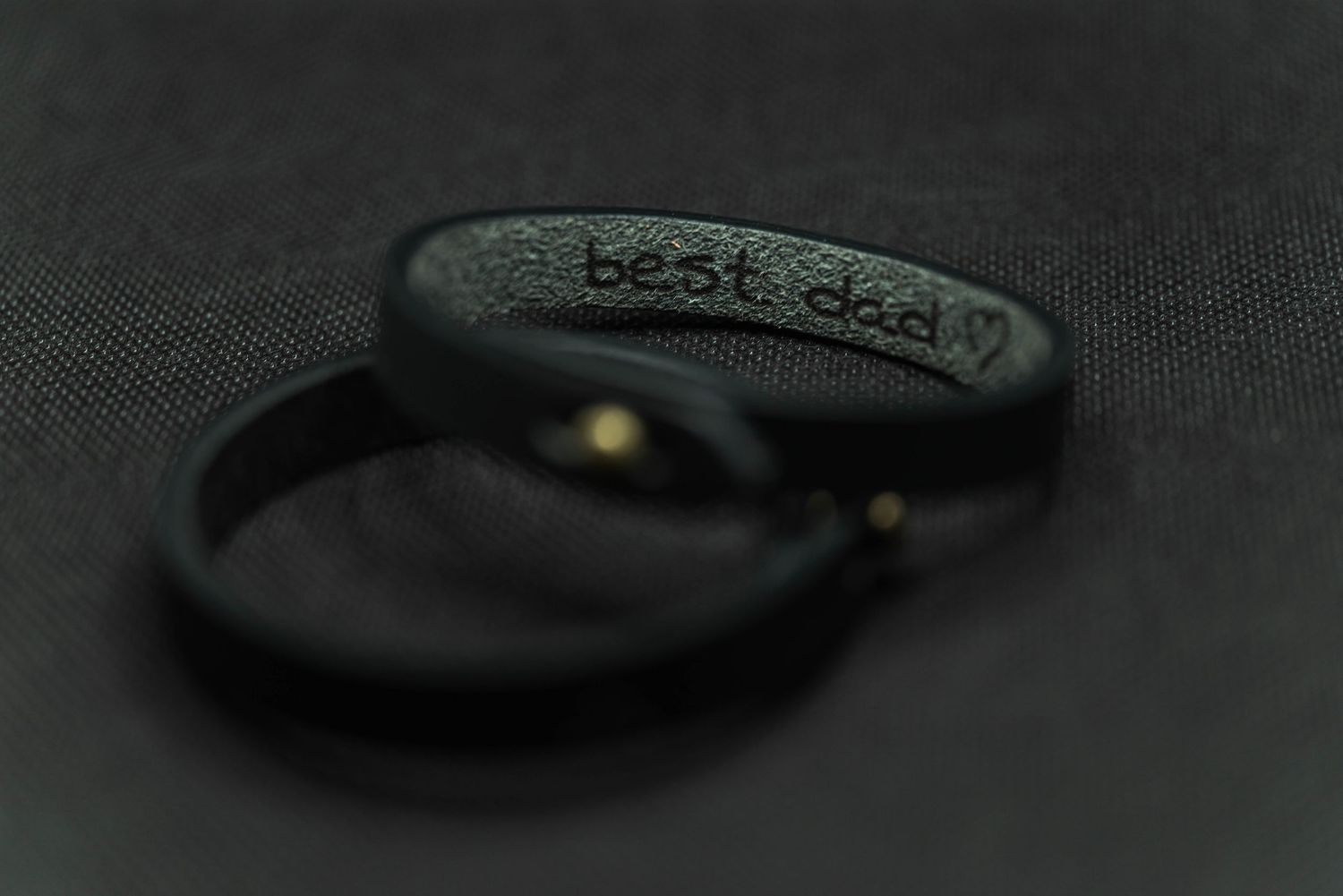 Two black leather bracelets with best dad engraving on dark fabric background.