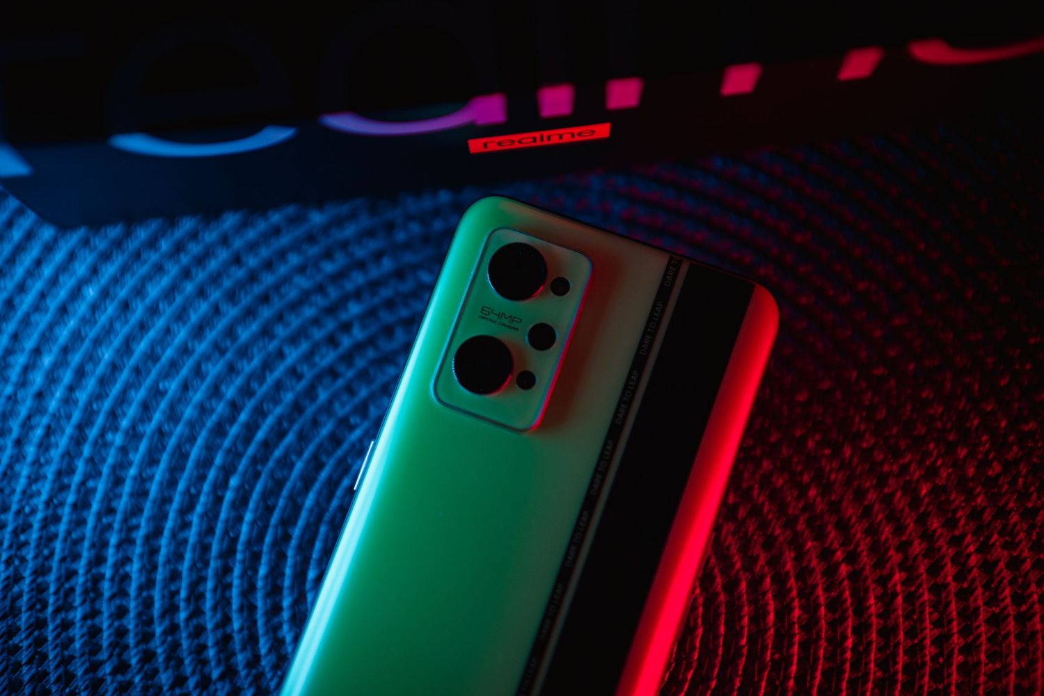 Close-up of Realme smartphone back panel with triple camera array under red and green neon glow.