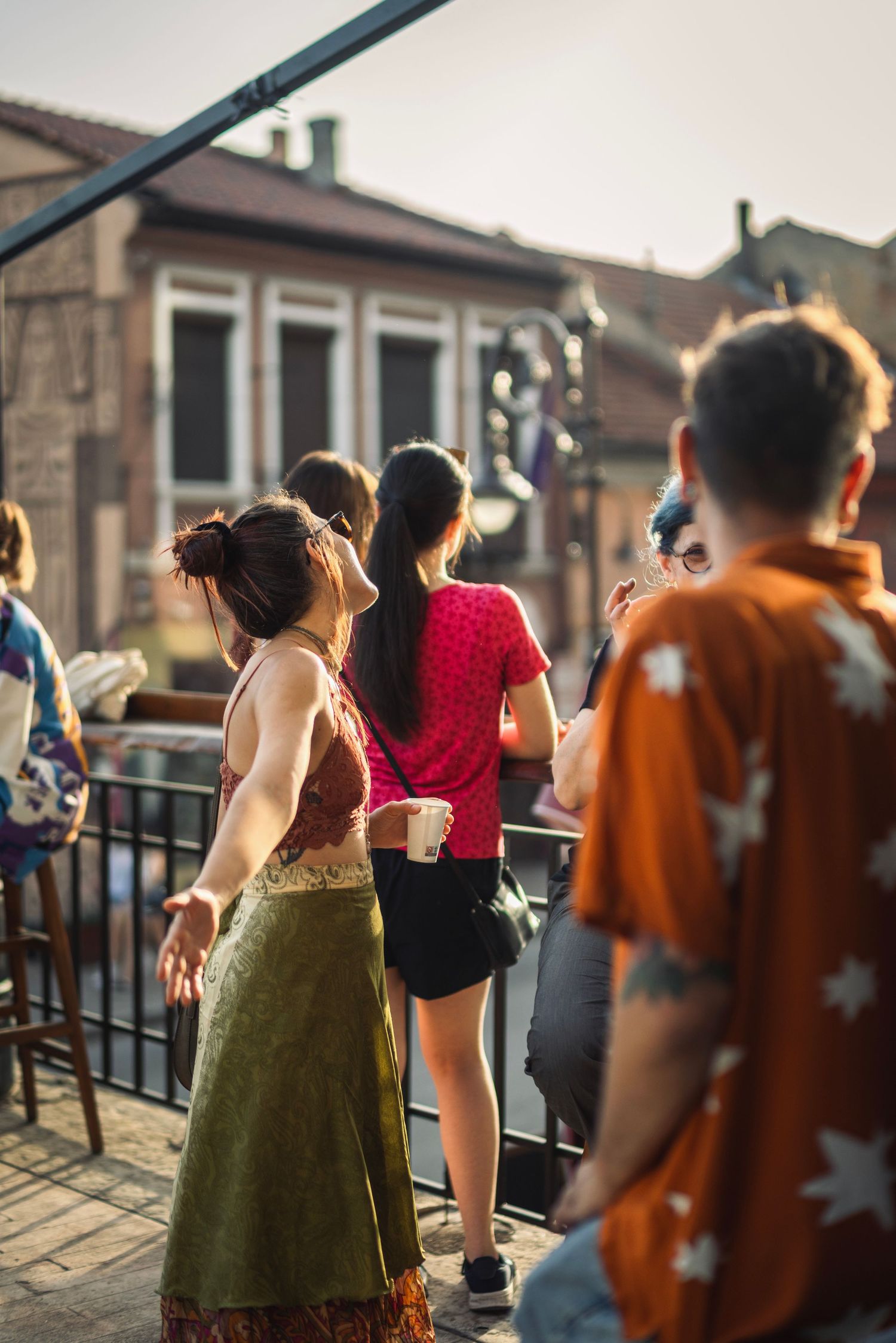 Group of young people socializing on a sunny outdoor terrace with historic buildings in the background.