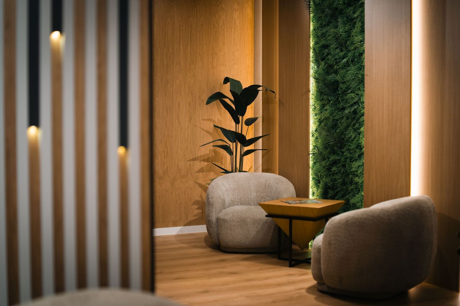 Elegant lounge corner with rounded beige chairs, indoor plant, and warm LED strip lighting on wood panels.