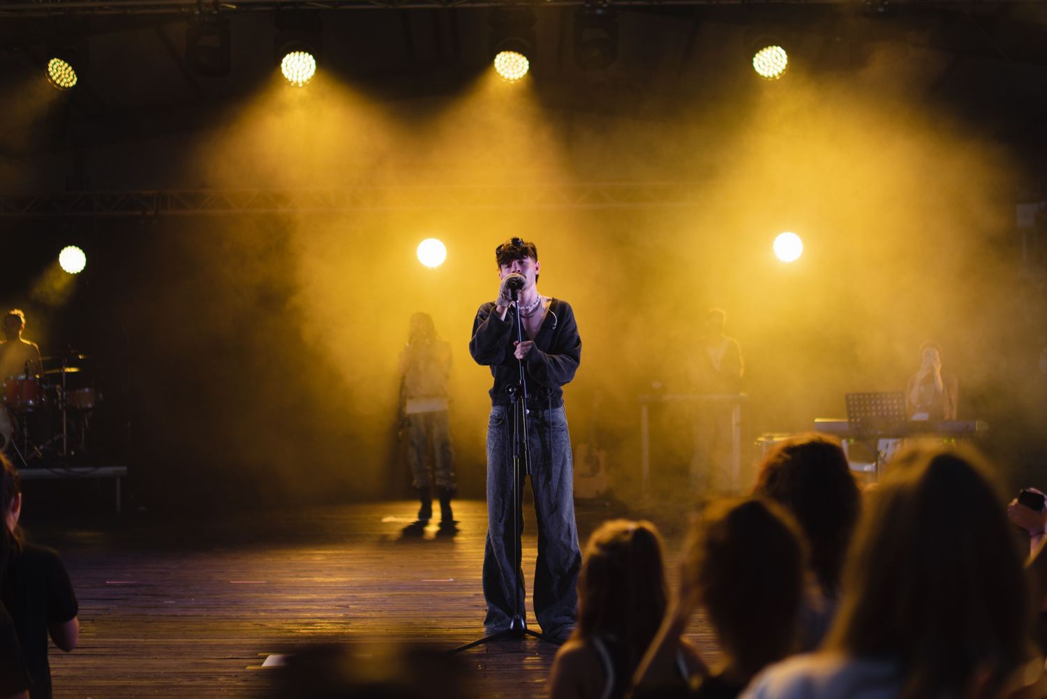 Solo performer on stage surrounded by yellow haze and bright stage lights with audience watching.