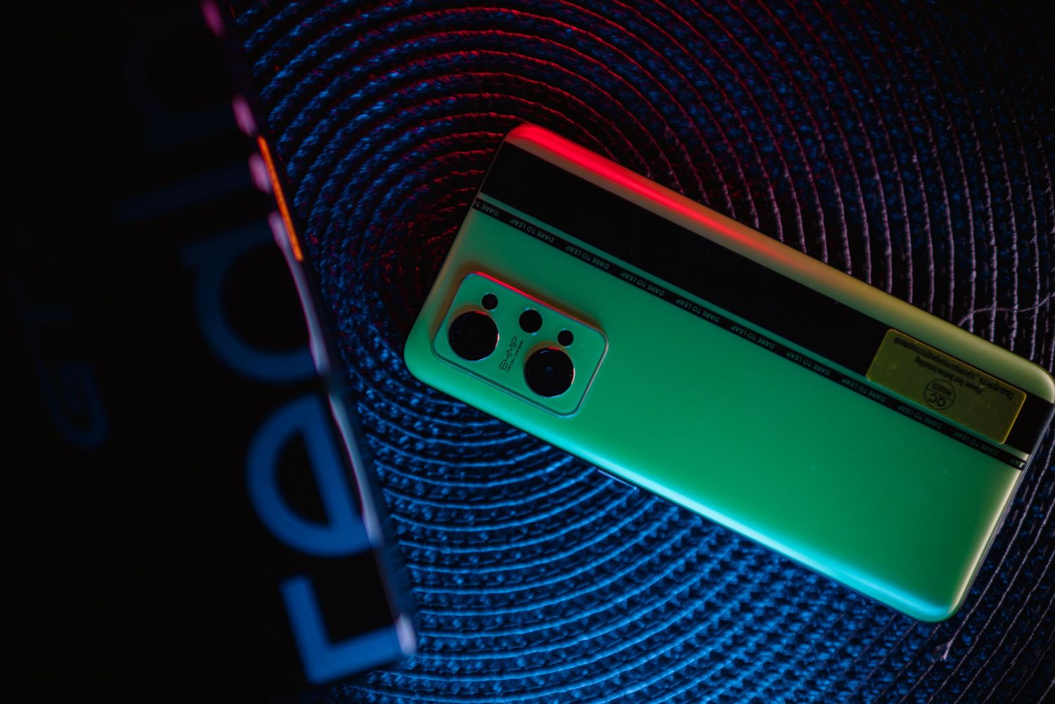 Realme phone rear camera module showcased with green gradient finish under colorful studio lighting.