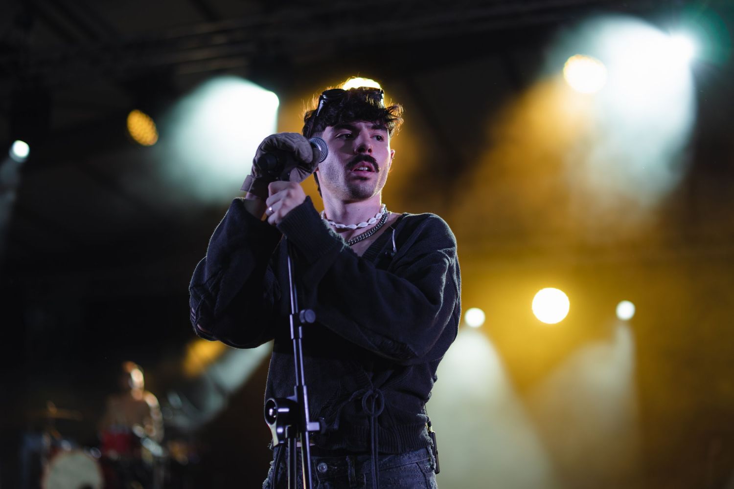 Male singer performing passionately at microphone under yellow stage lights at night concert.