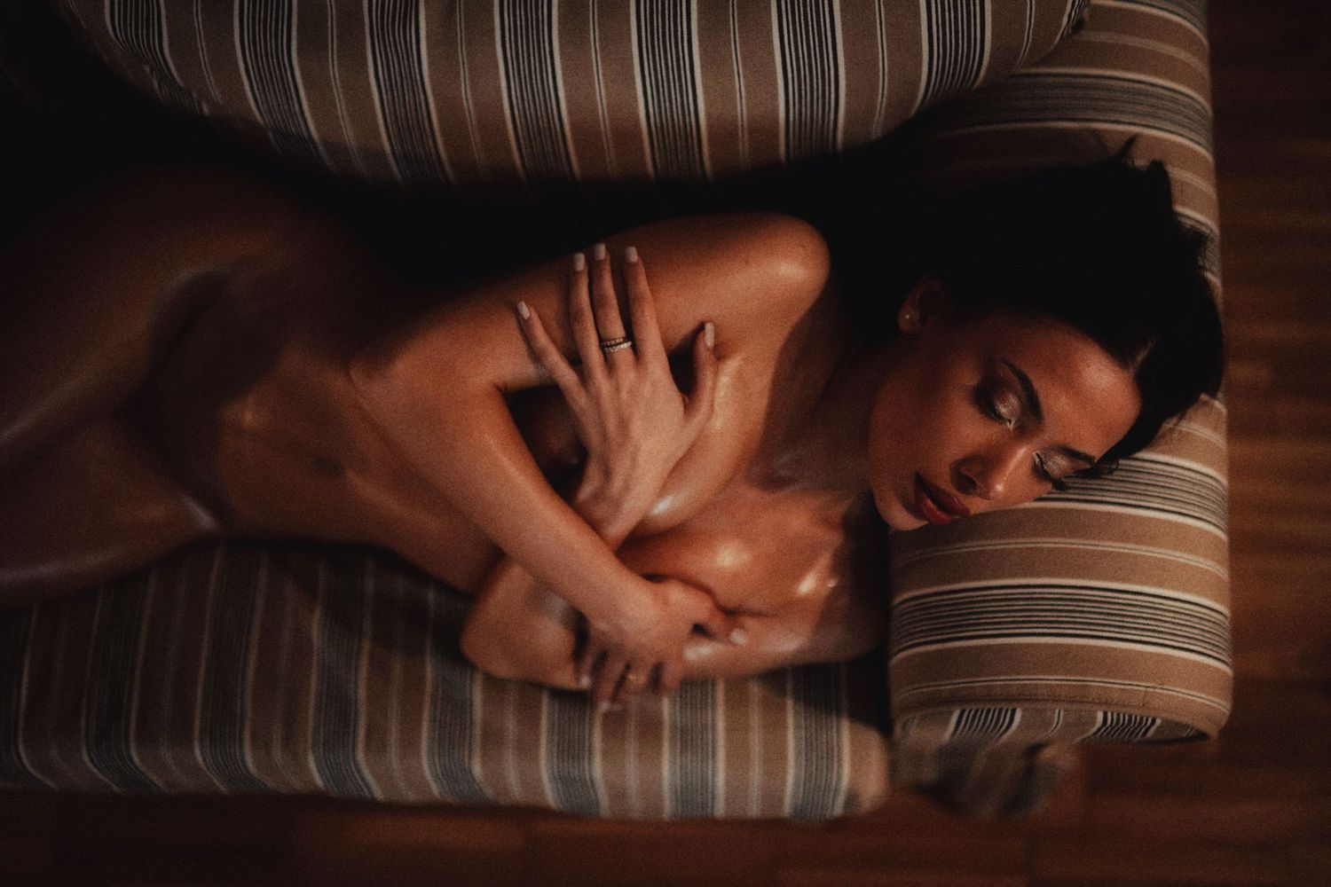 Woman lying on striped couch cushions in moody dark ambient lighting photography.