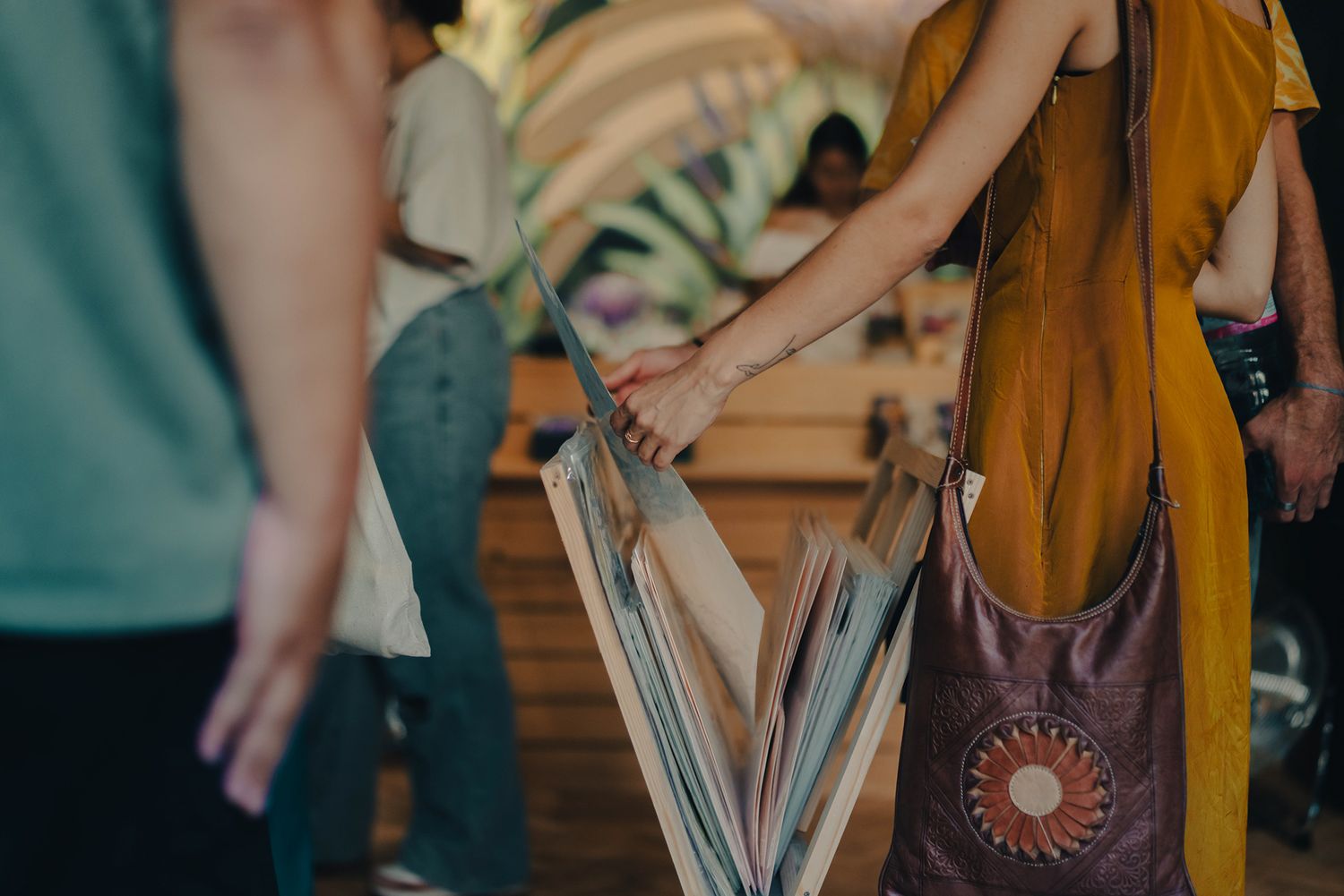 Person carrying folded umbrella and brown boho shoulder bag at an outdoor festival event.