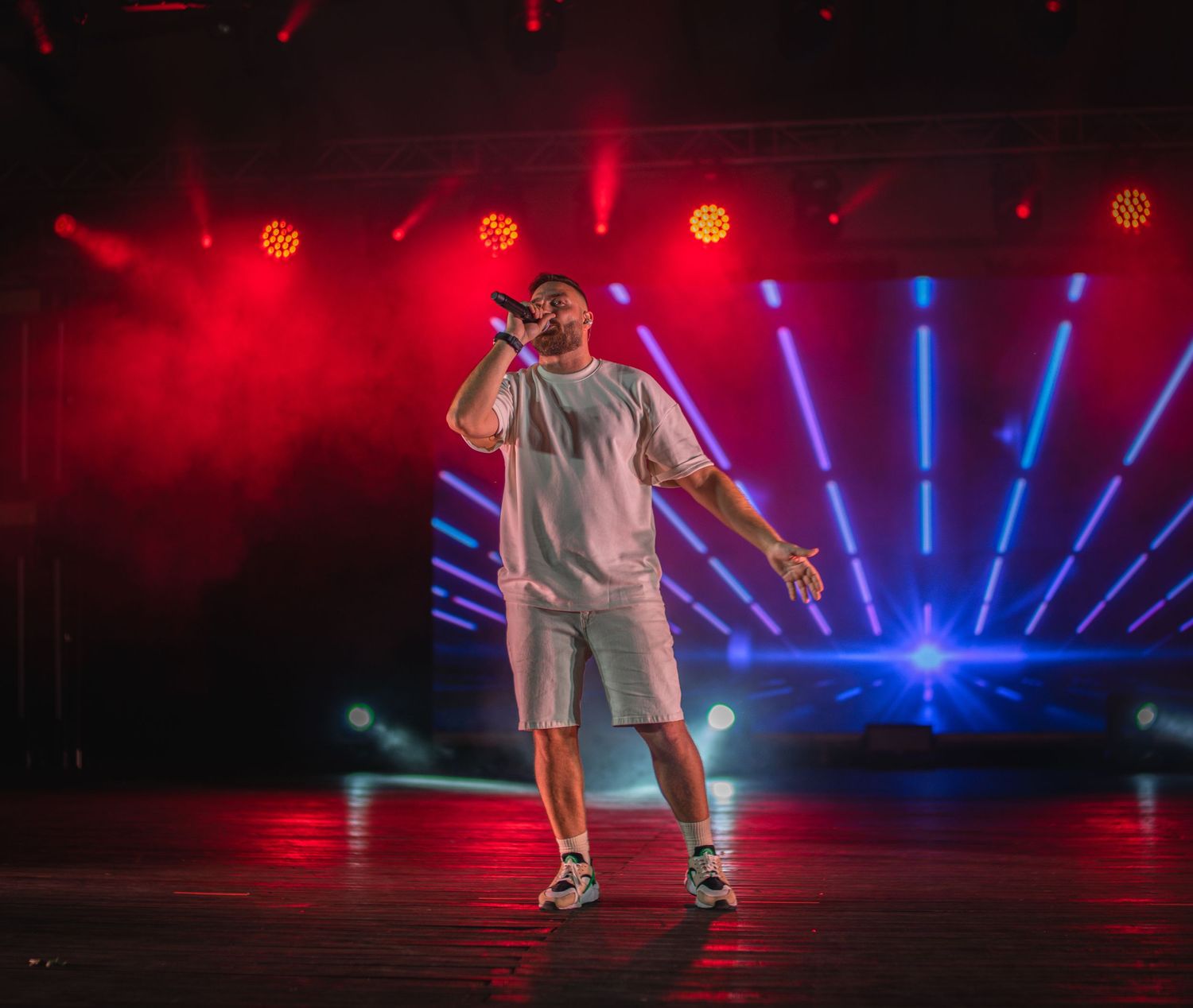 Solo performer in white outfit singing under dramatic red and blue stage lights with light rays.