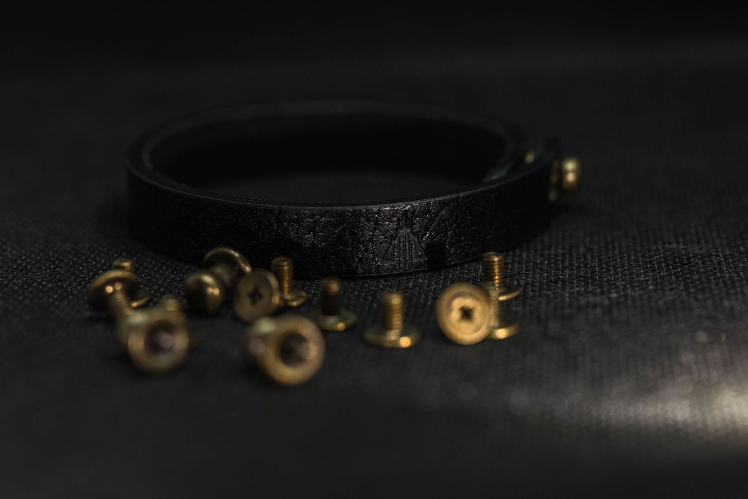 Black leather bracelet with brass rivets scattered around on dark textured fabric background.