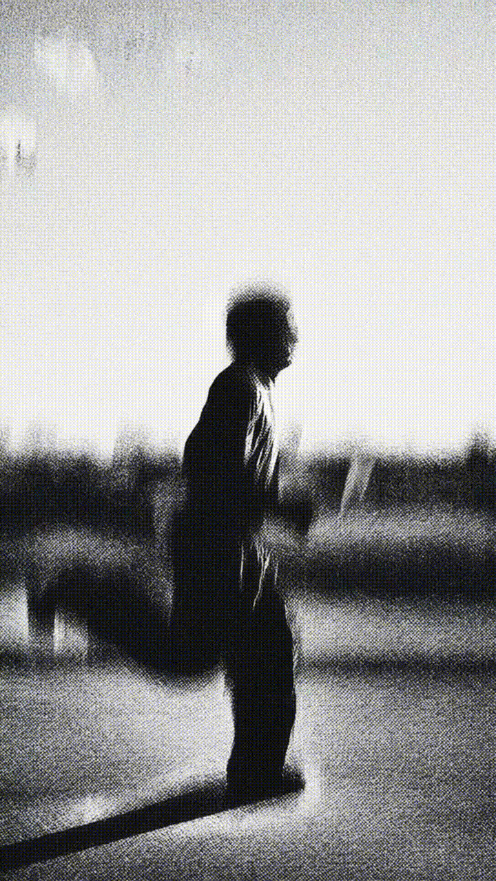 Silhouette of a man standing outdoors in dramatic grainy monochrome light, conveying solitude and contemplation.
