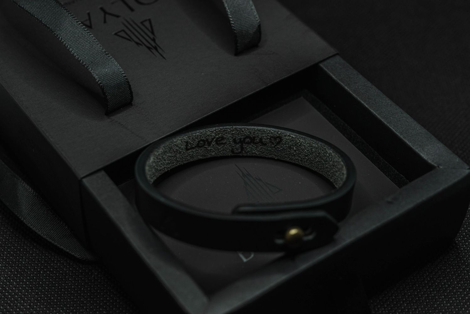 Black leather bracelet with engraved message inside dark luxury gift box with branded tissue paper.