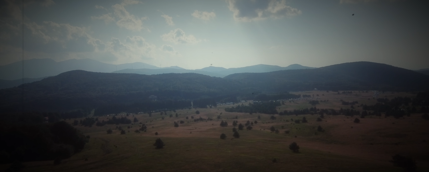 Wide aerial panorama of rolling green mountain valley under cloudy sky.