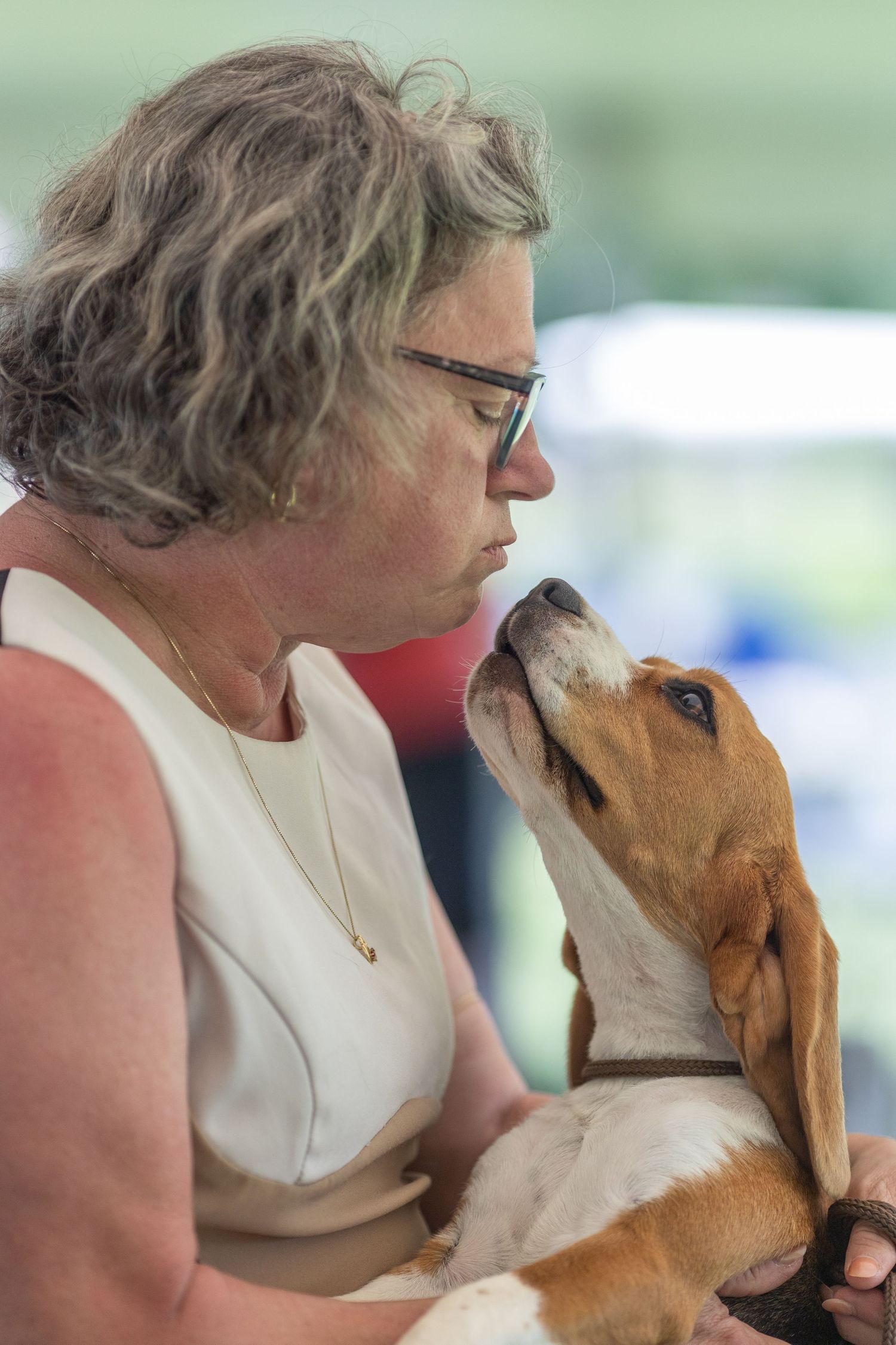 Woman in white dress sharing a tender nose-to-nose moment with a beagle puppy she holds in her arms.