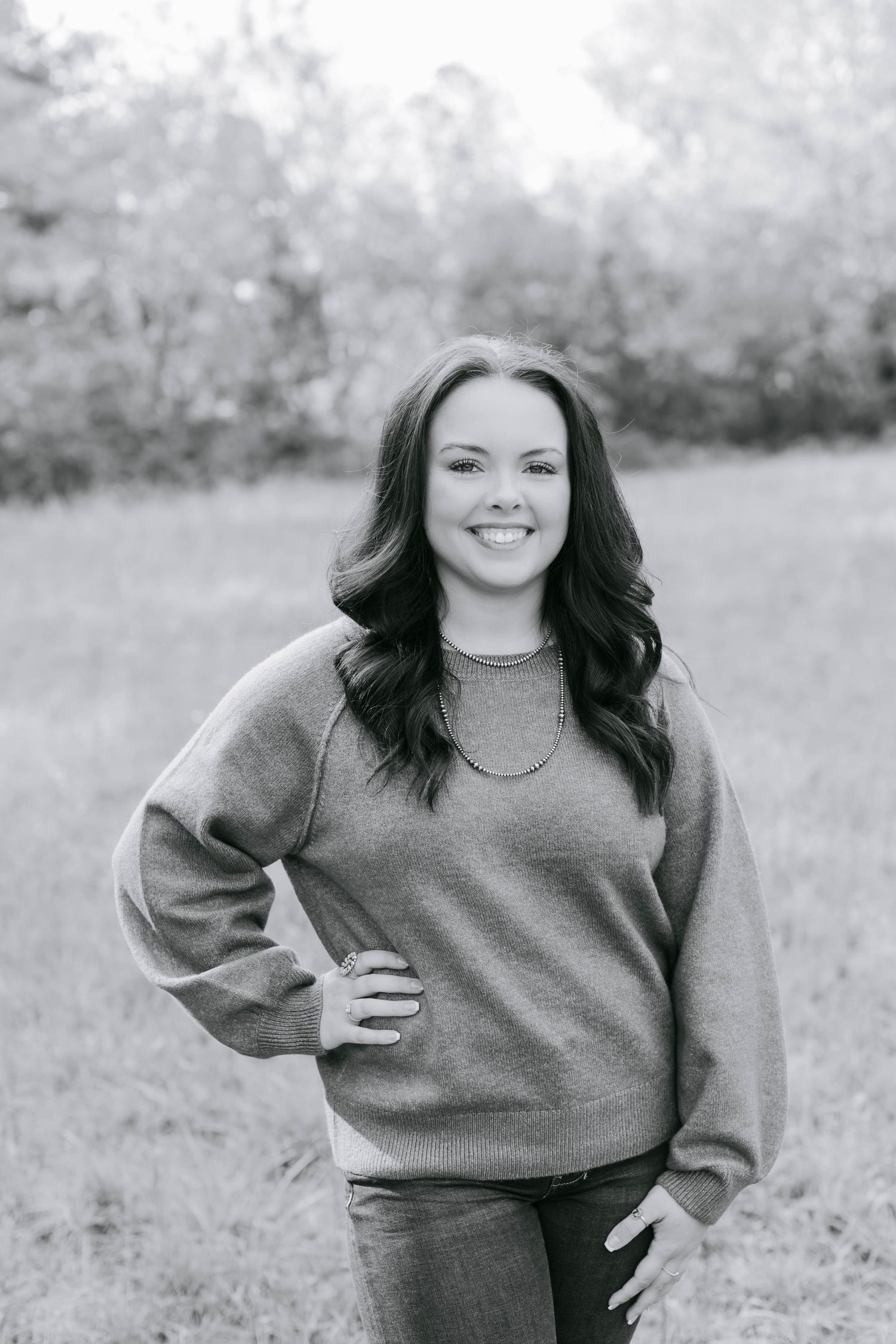 Black and white portrait of smiling brunette woman in sweater posing outdoors.