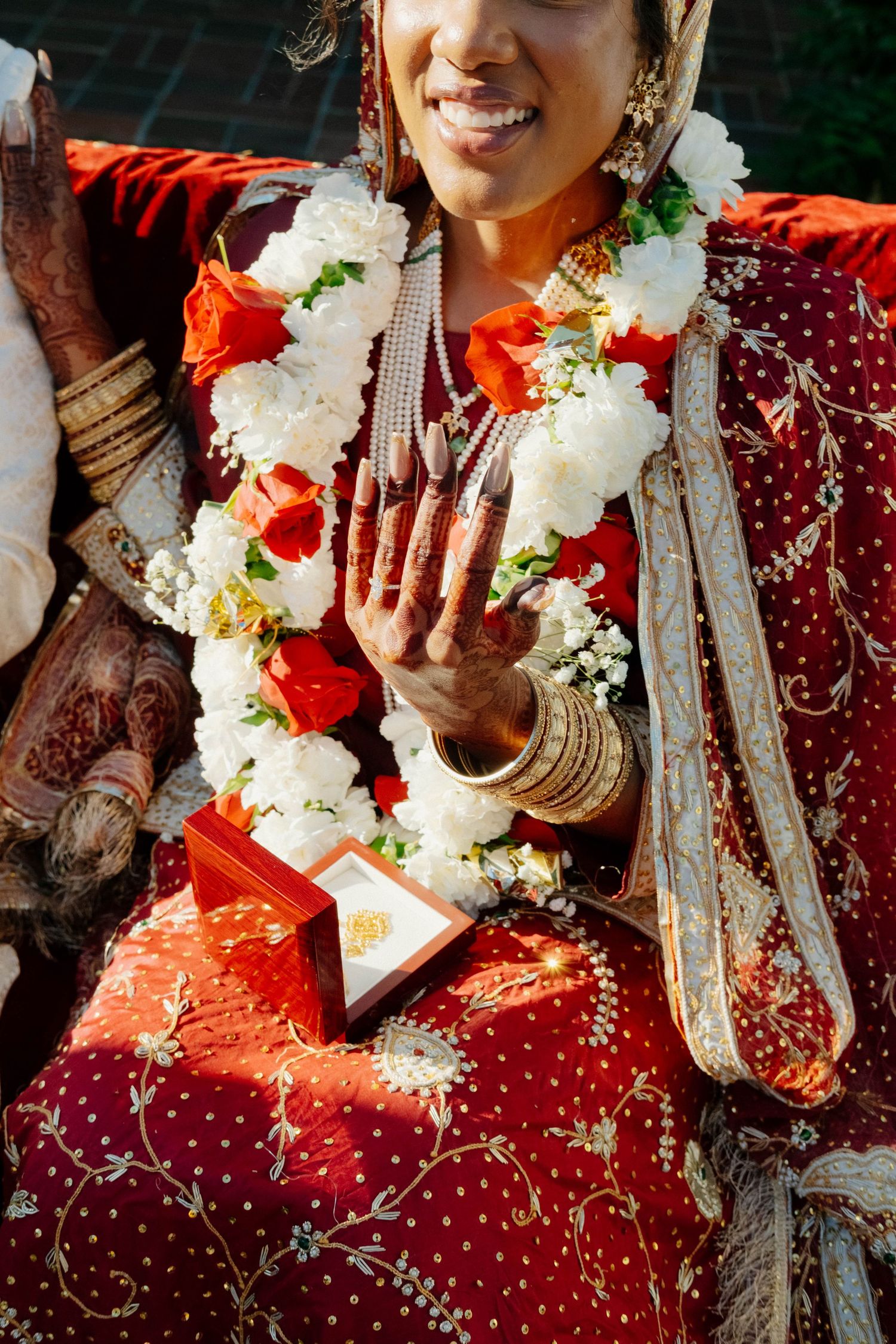 A close-up shot highlights the bride's intricate henna designs and gold jewelry on her hand while she displays her ring.