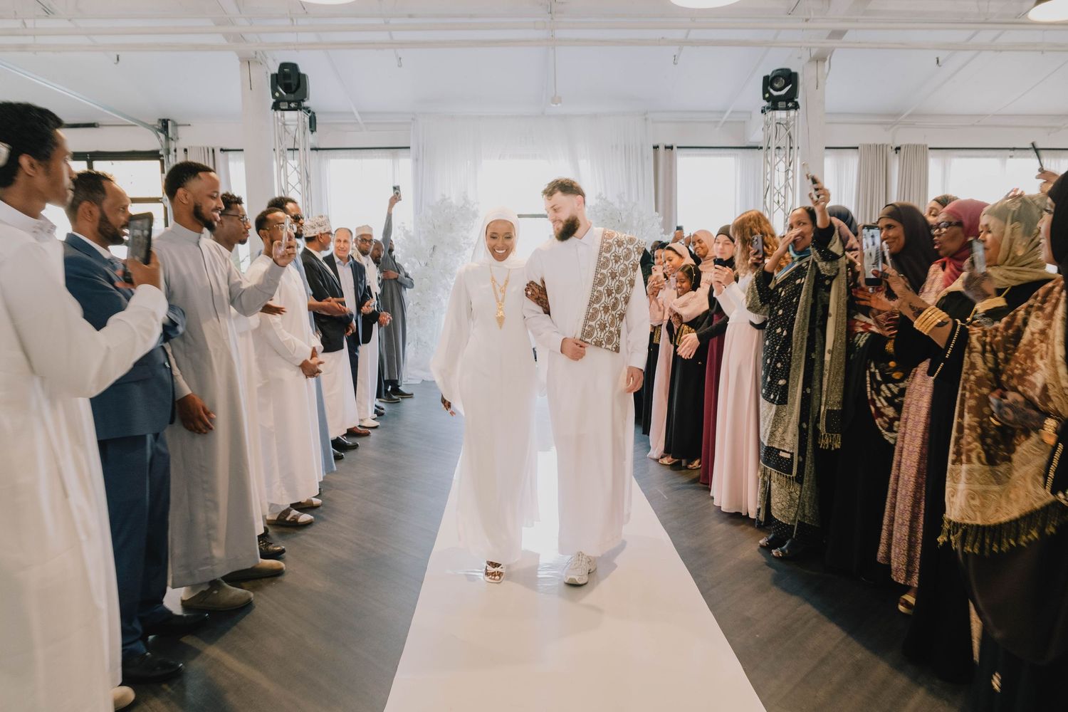 A wide shot shows the couple walking down the aisle, surrounded by guests capturing the moment.