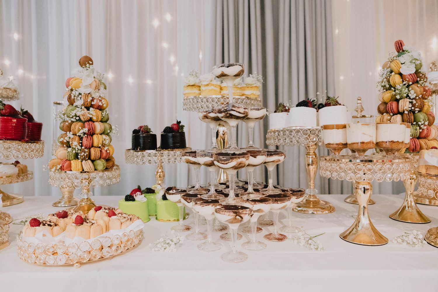 An elaborate dessert table is elegantly decorated with tiered sweets, macarons, and small cakes.