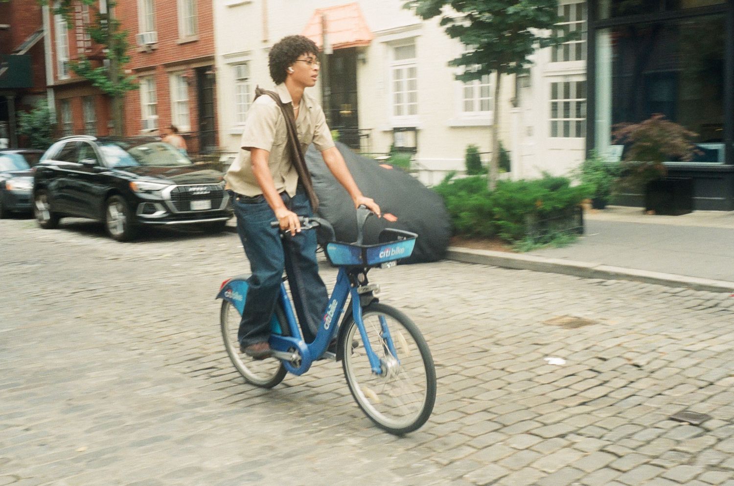 A person rides a blue rental bicycle along a city street.