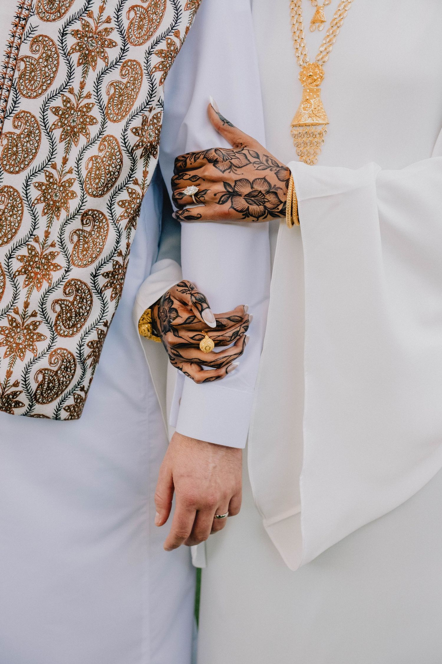 A close-up captures the couple holding hands, highlighting the bride's intricate henna and gold jewelry.
