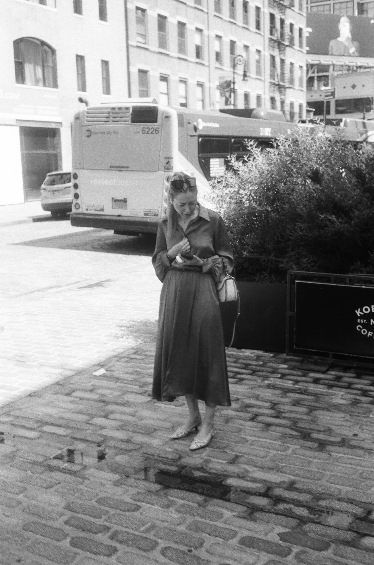 A woman in a long dress stands on a cobblestone street.