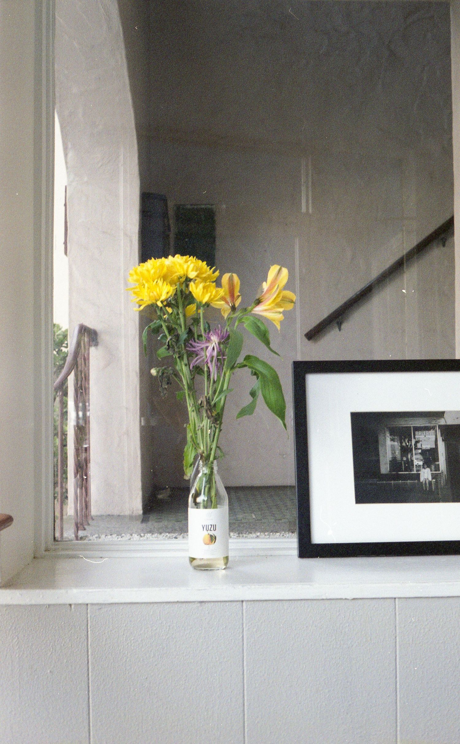 A bunch of yellow flowers in a vase on a windowsill.