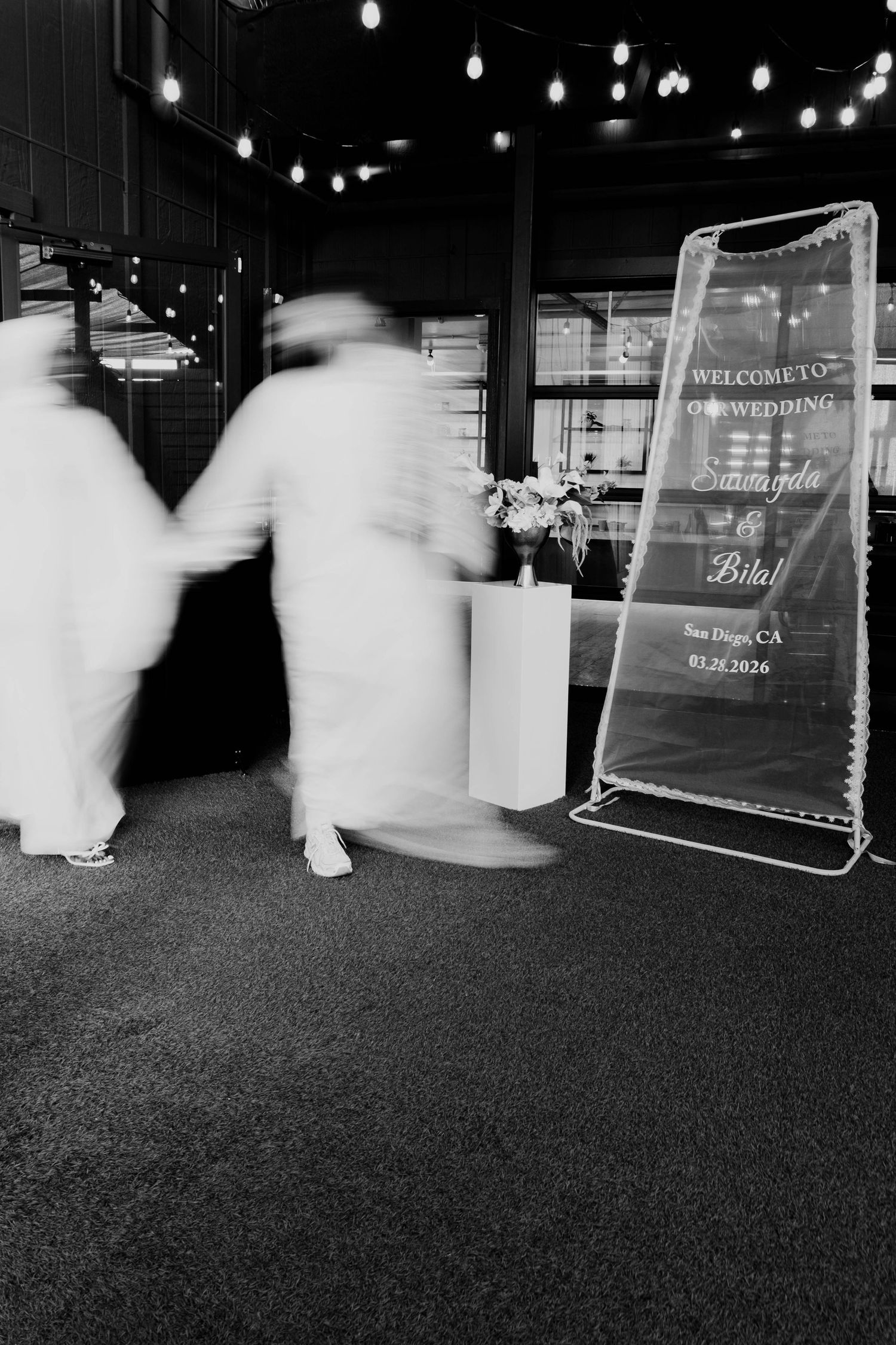 A motion-blurred image captures the couple walking past a wedding welcome sign.