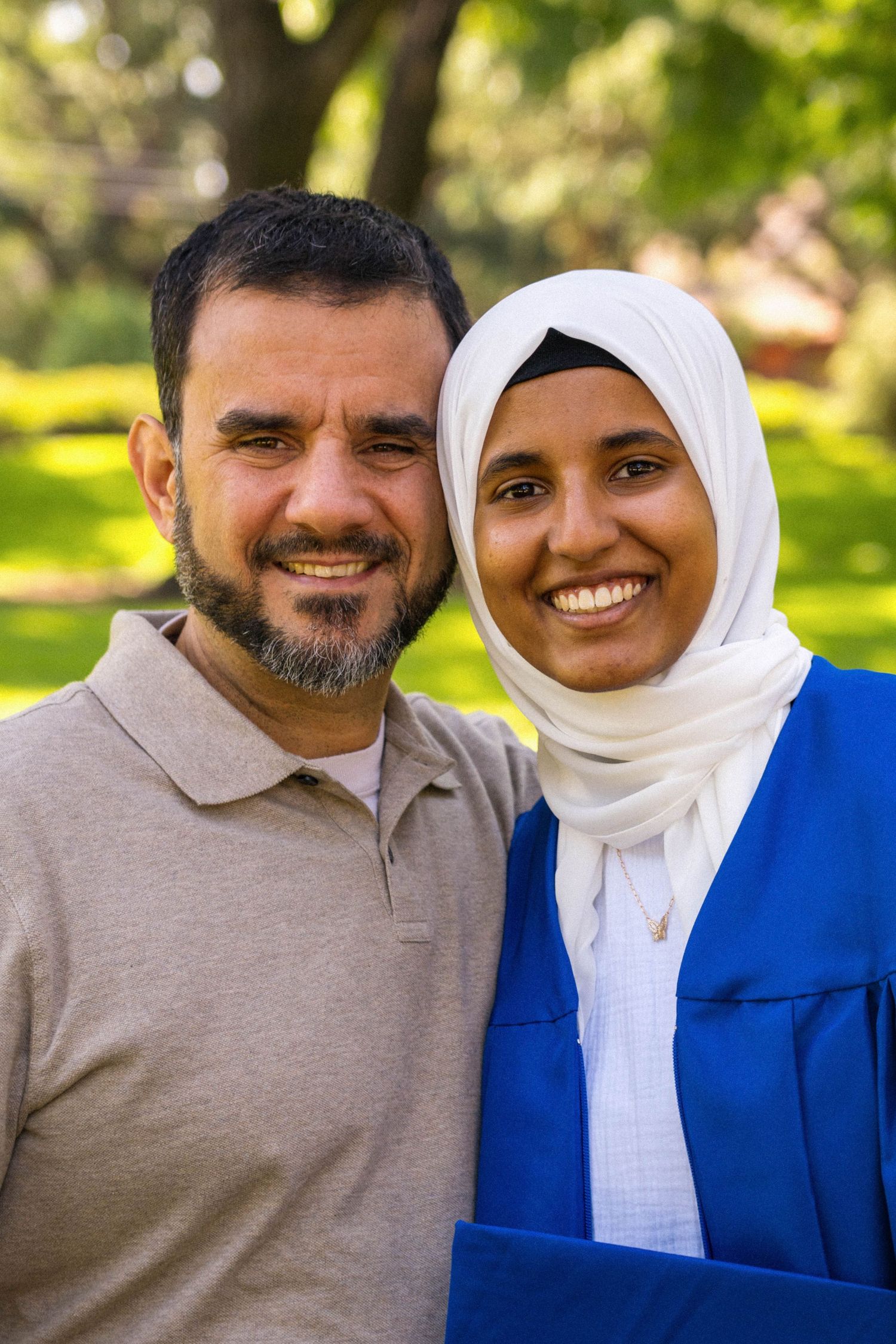 A man smiles while standing next to a graduate in blue robes.