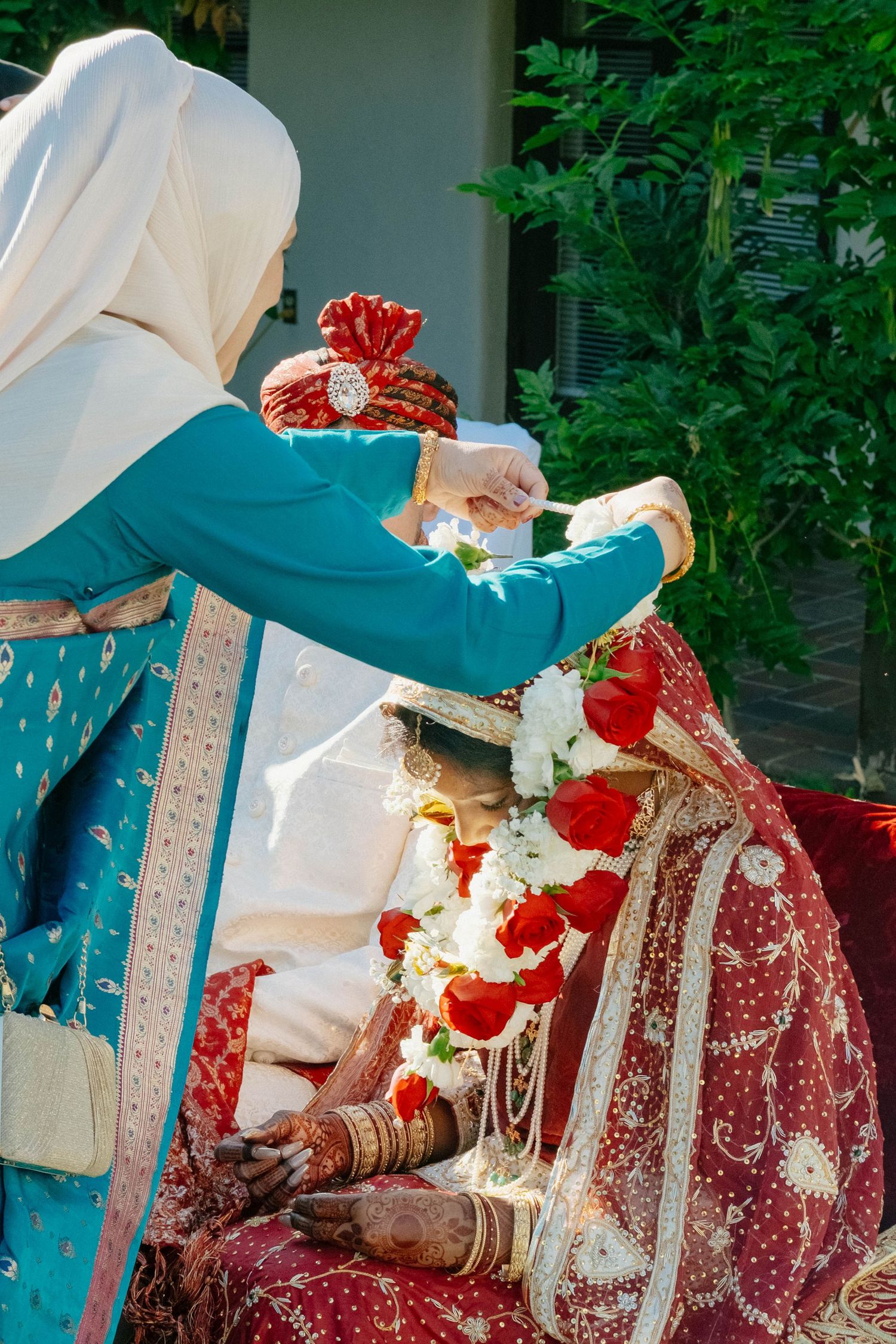 A guest performs a traditional ceremony, placing a floral garland over the bride's head.