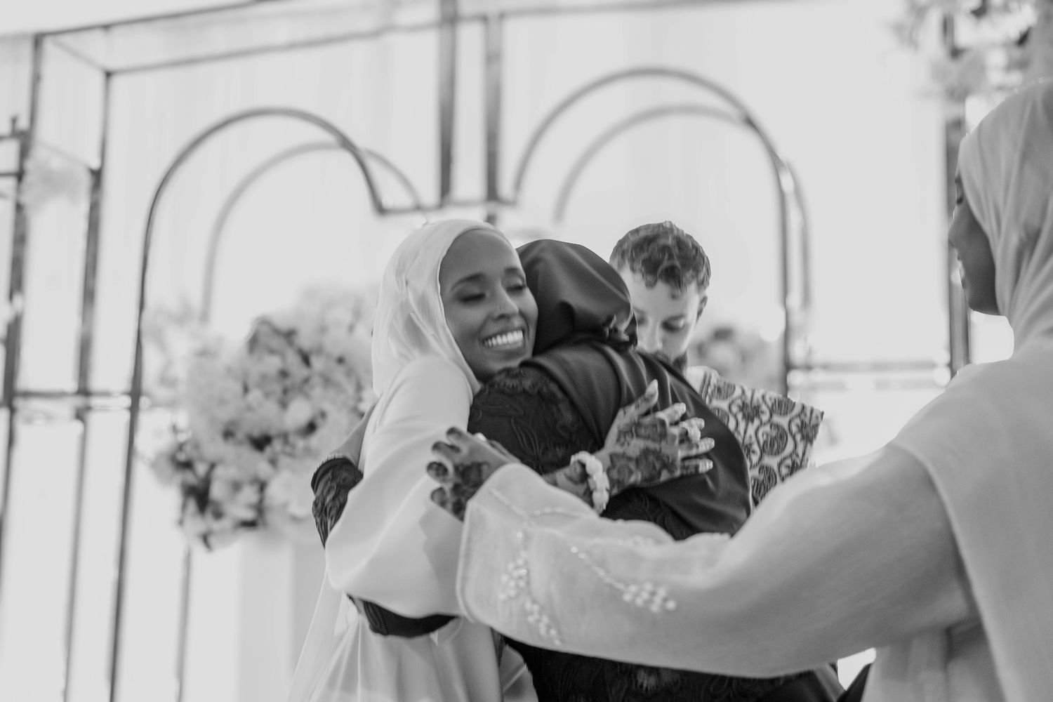 Two individuals embrace warmly in a heartfelt, black-and-white wedding moment.