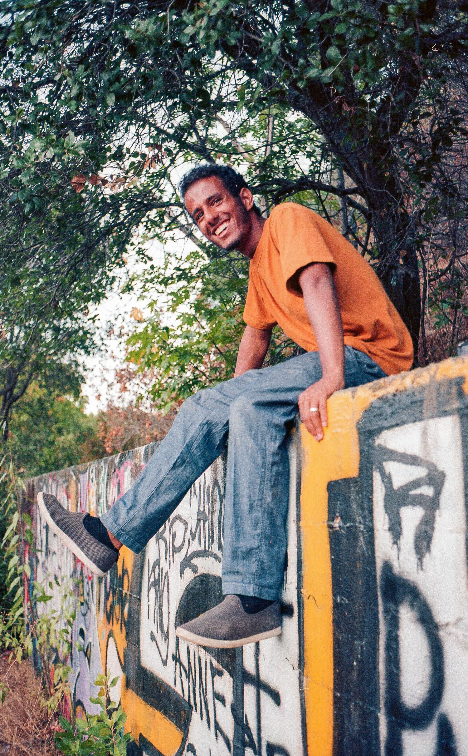 Young man sitting on a graffitied wall.