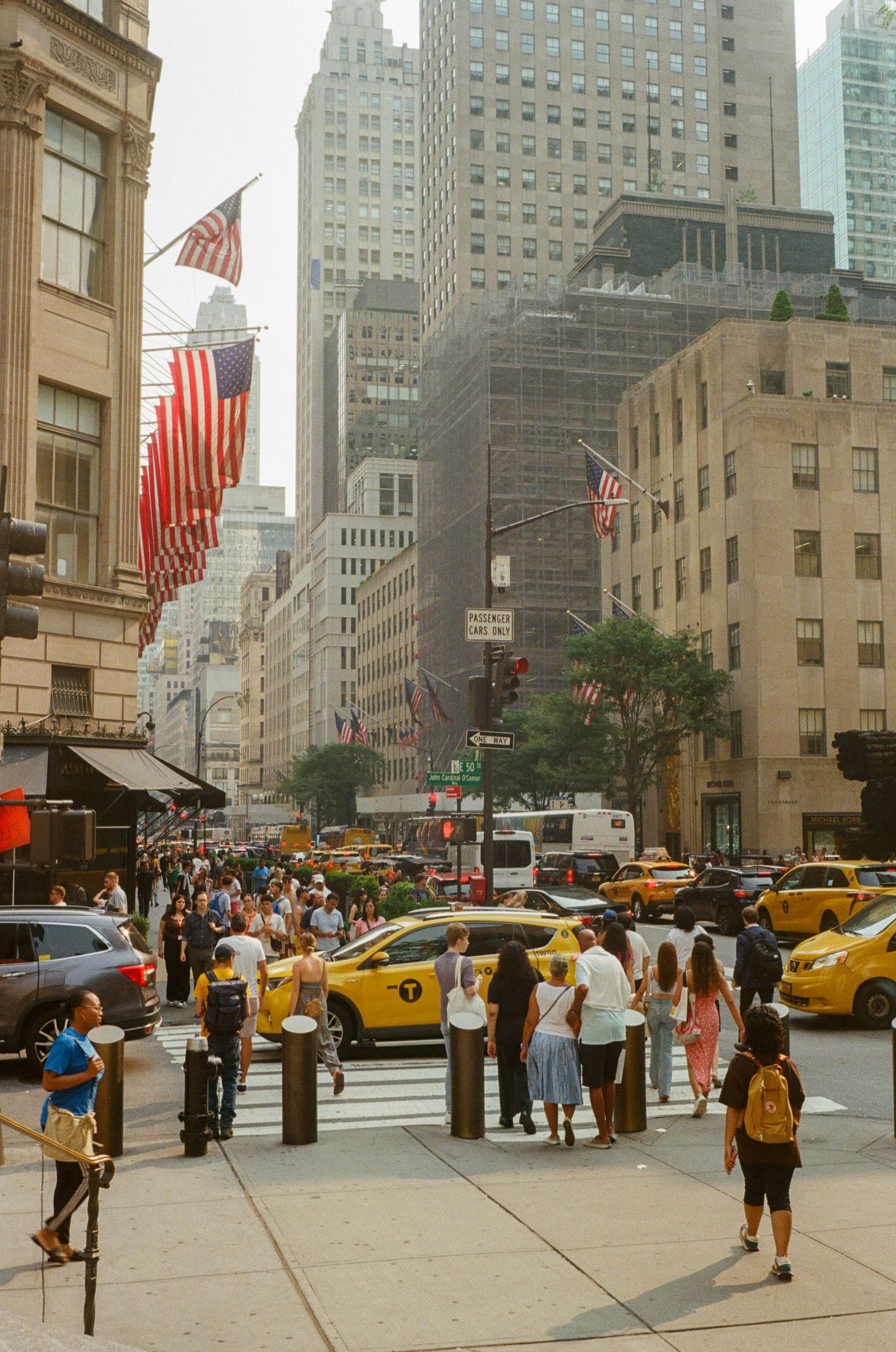 Crowds of people cross a busy New York City street.