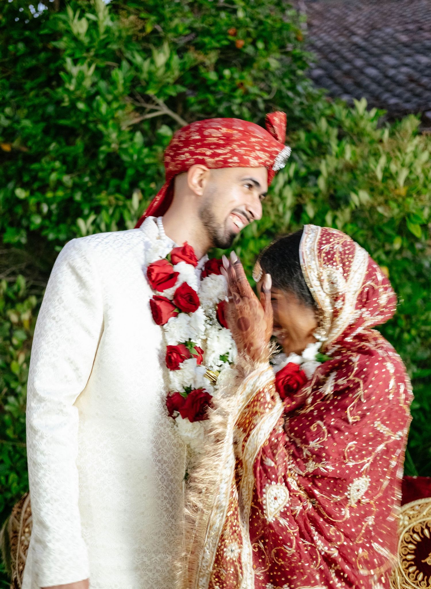 A couple in traditional wedding clothes embrace during a celebration outdoors.