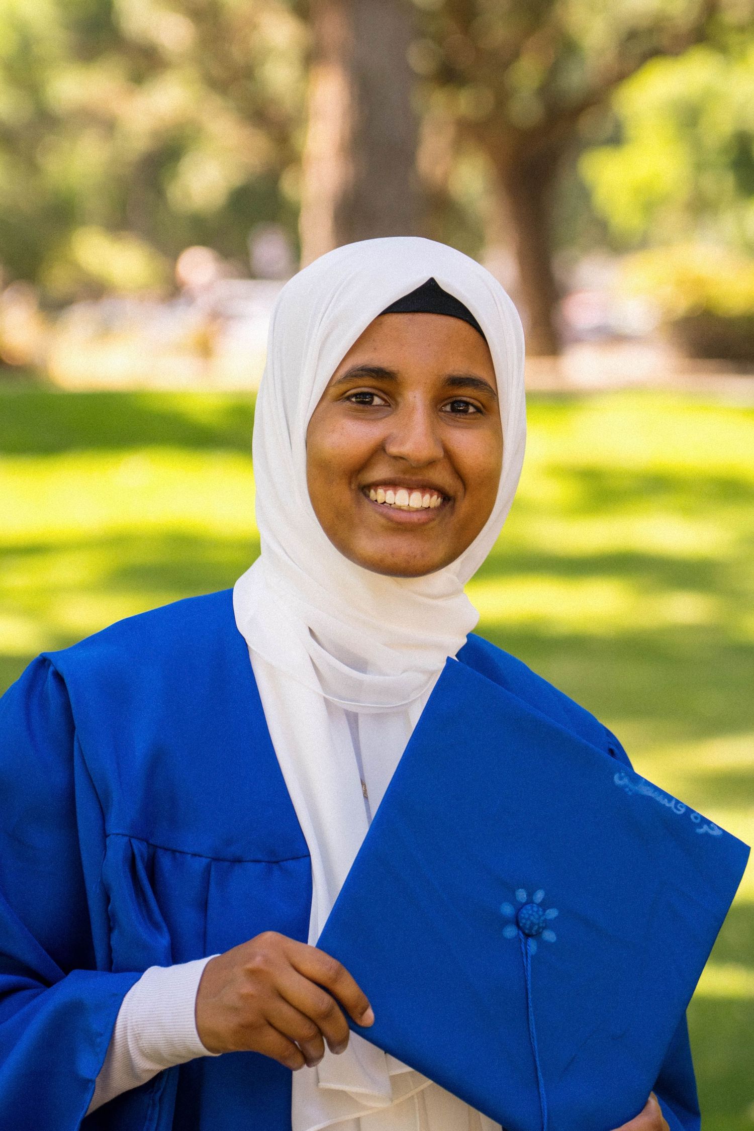 A happy graduate smiles while holding her blue cap and gown ensemble.