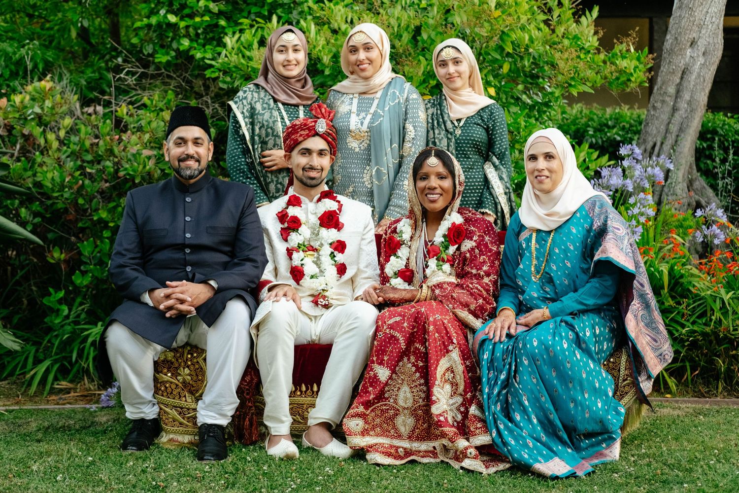 The wedding party and family members pose for a portrait in an outdoor garden setting.