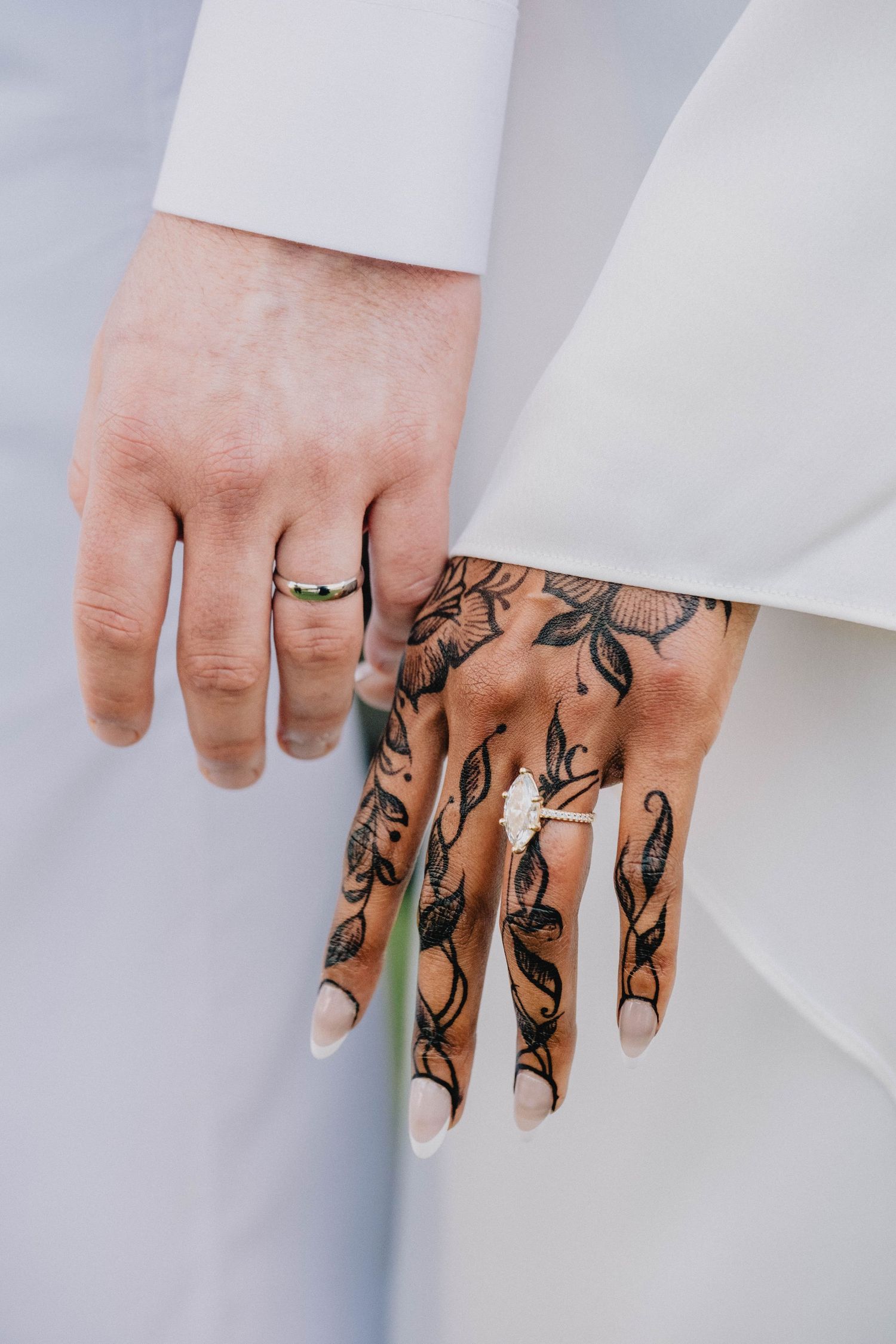 The couple holds hands, showcasing the bride's detailed floral henna design and diamond engagement ring.