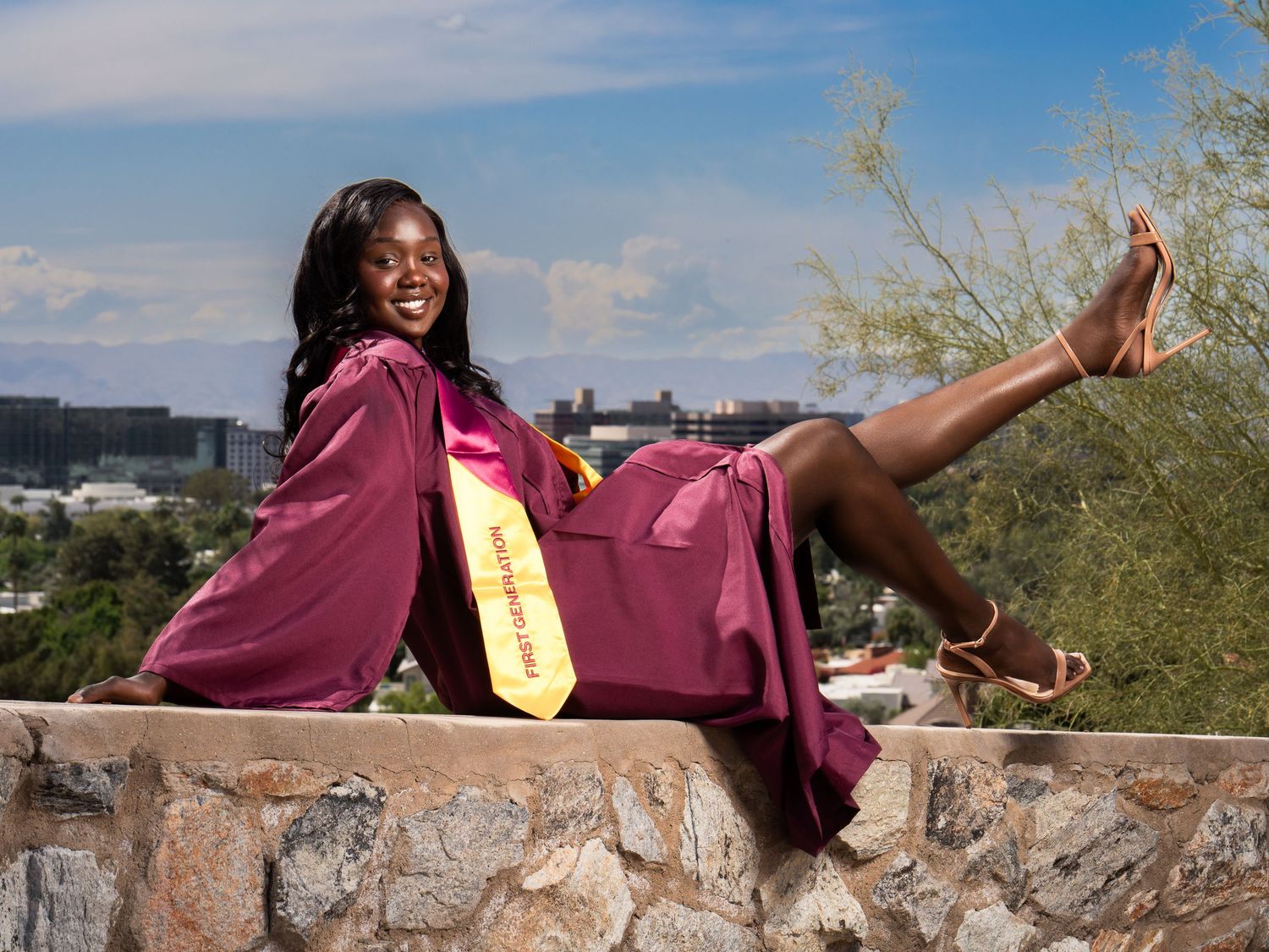 Graduate in a maroon cap and gown celebrating outdoors in Phoenix.Graduate in a maroon cap and gown celebrating outdoors in Phoenix.