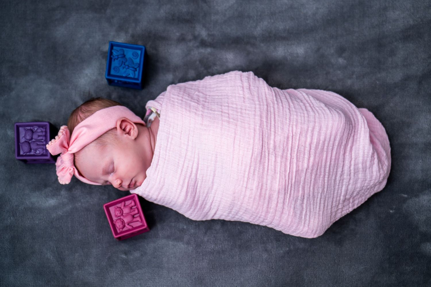 Newborn wrapped in pink and posed with colorful letter blocks.