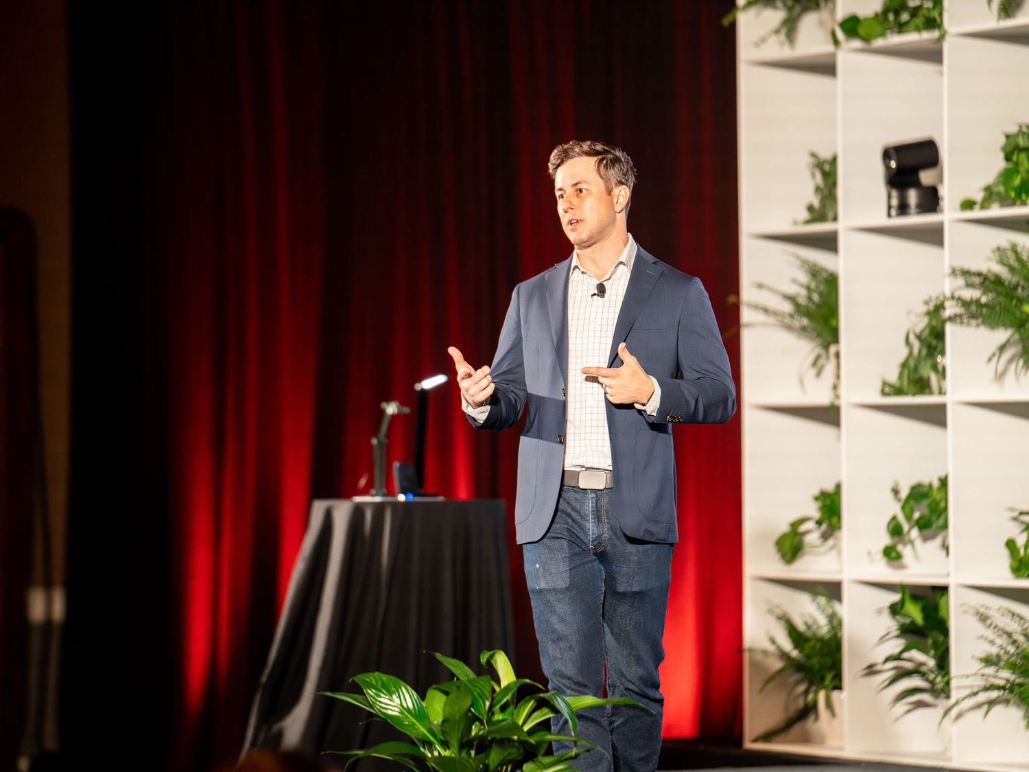 Business speaker presenting onstage against red curtains during a corporate event.