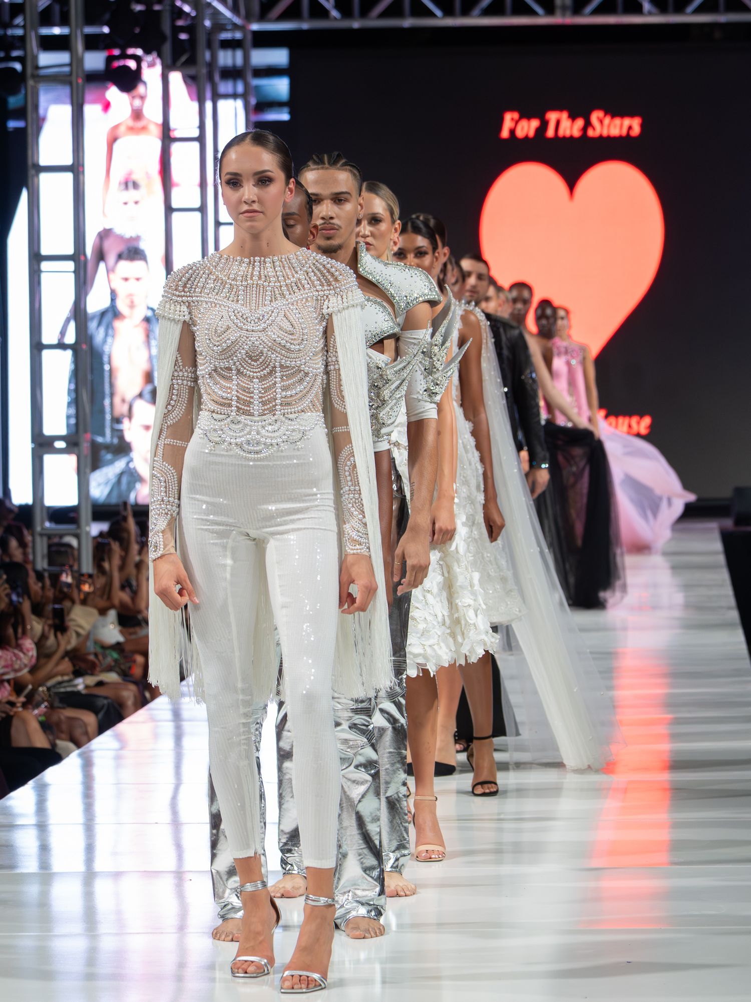 Event guests posing together in a photo booth with colorful novelty glasses.Models in white designs walking the runway during a fashion even