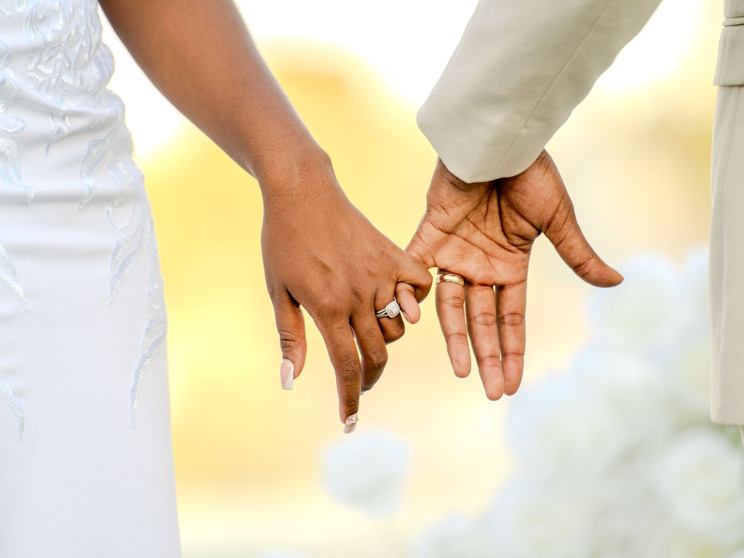 Close-up of bride and groom holding hands showing wedding rings during outdoor ceremony.