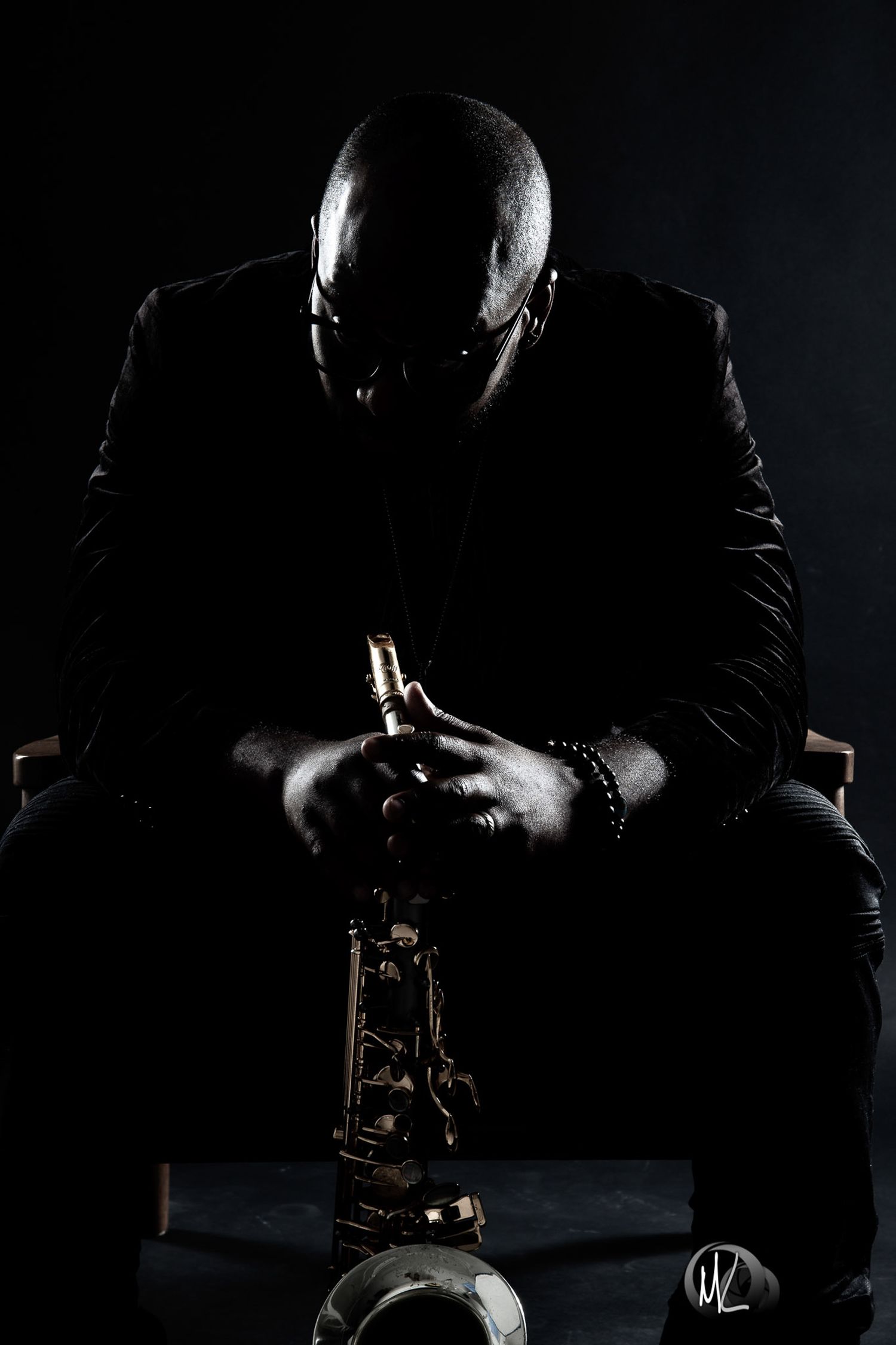 Low-key portrait of a man in a dark suit seated with clasped hands.