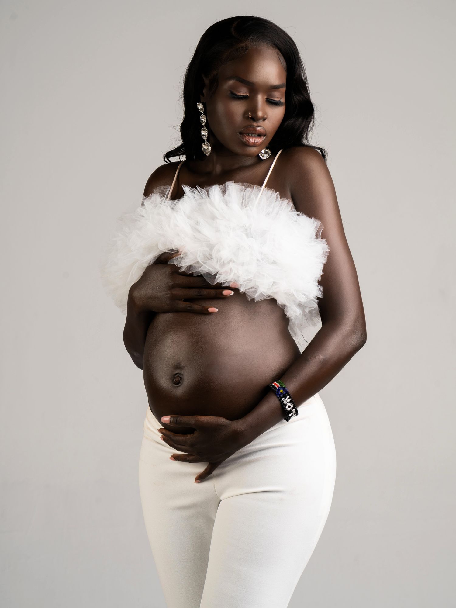 Expectant mother in white maternity attire posing against a neutral studio backdrop.