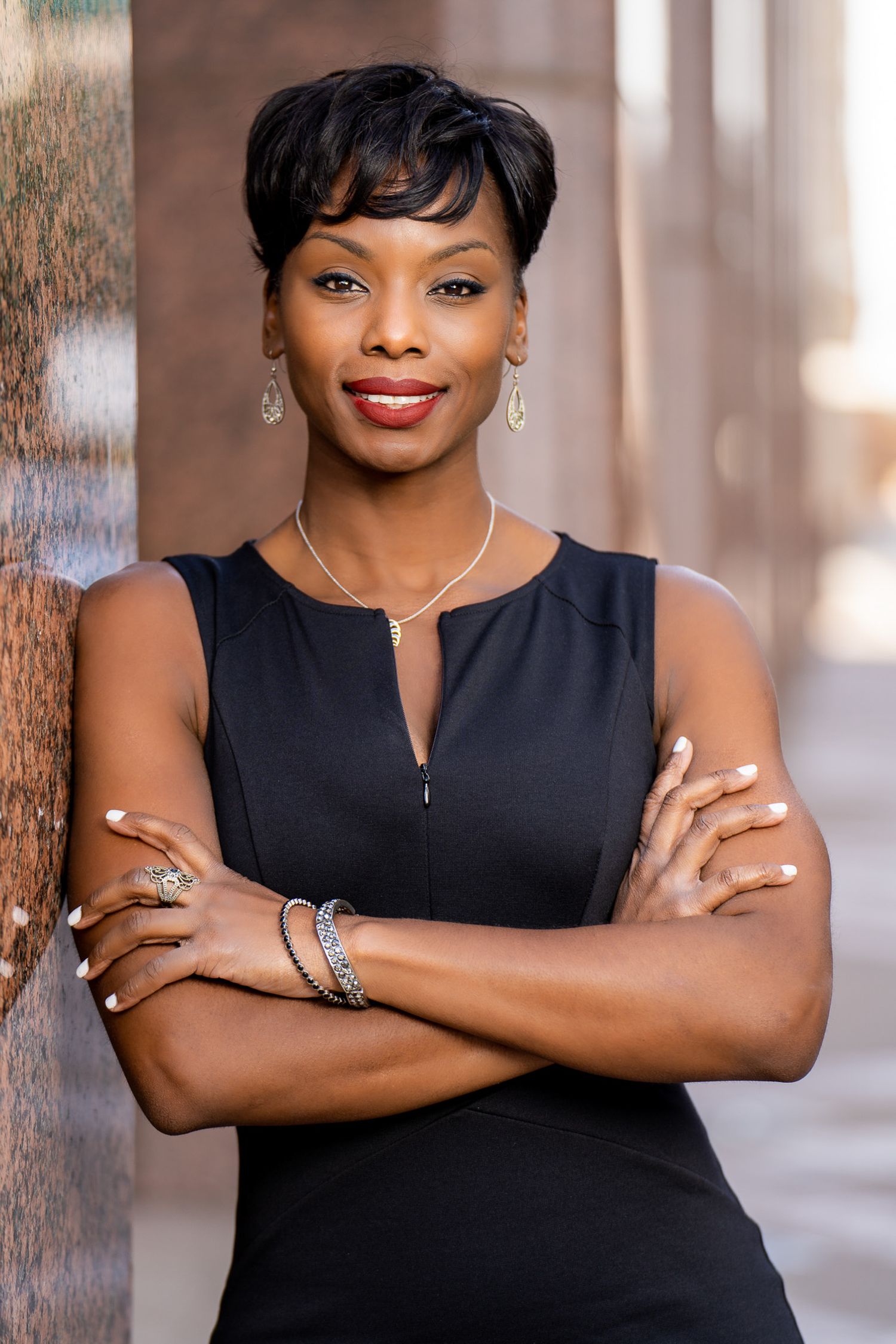 Confident woman in a sleeveless black dress posing with folded arms.