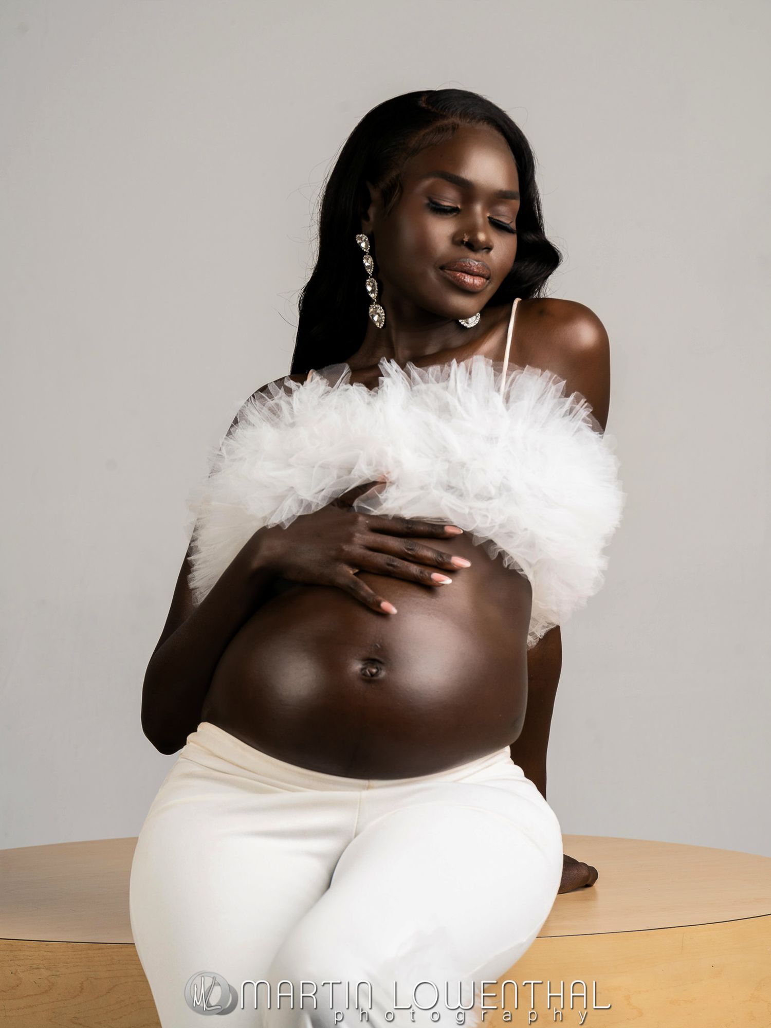 Expectant mother in white maternity attire posing against a neutral studio backdrop.