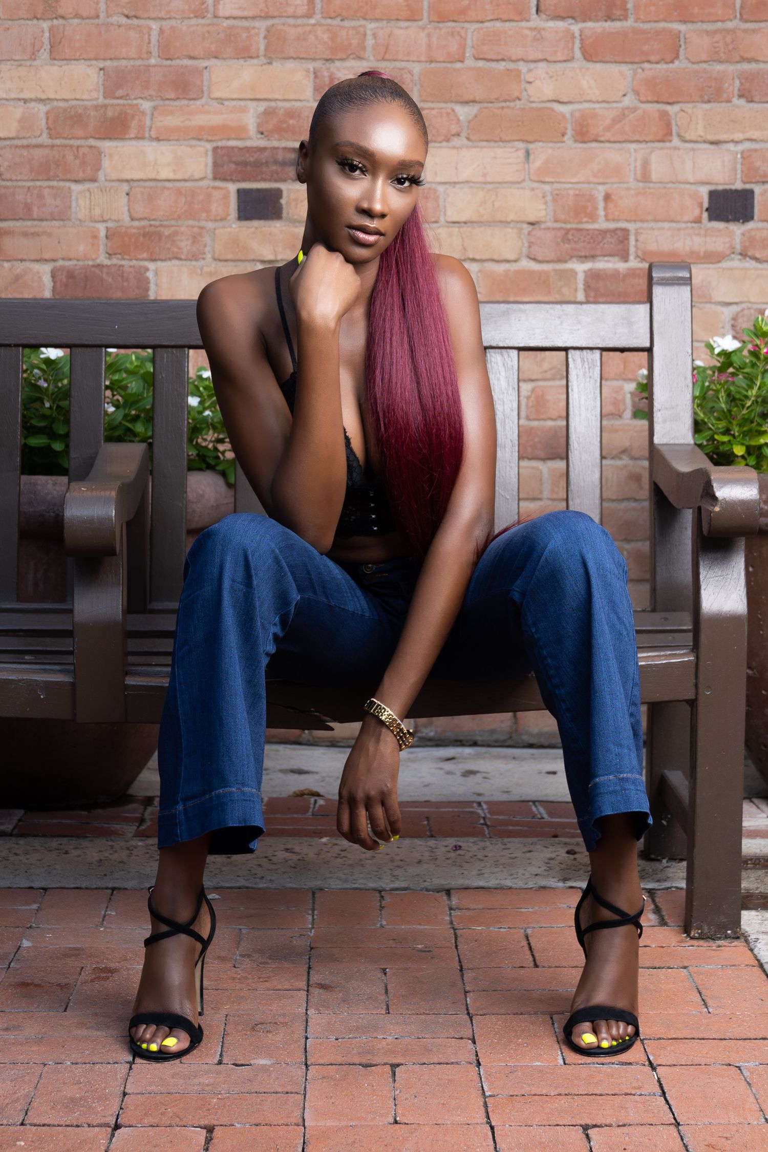 Confident woman in a burgundy top and jeans seated against a brick wall.